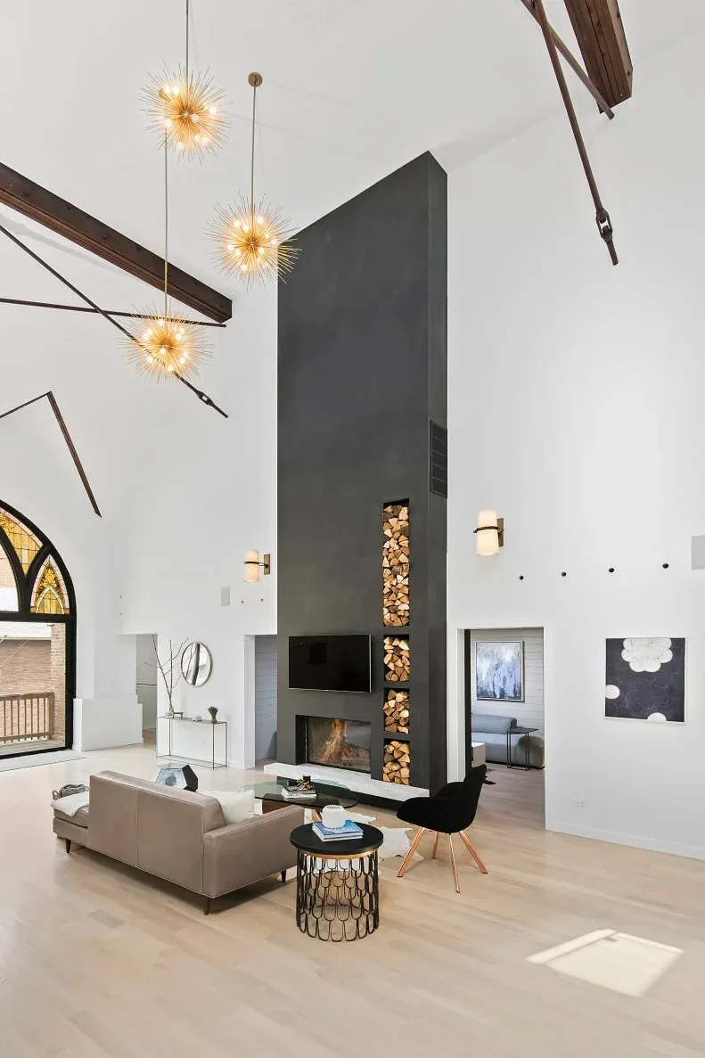 Very tall charcoal fireplace column under pitched white ceiling with narrow log recess and pale sofa