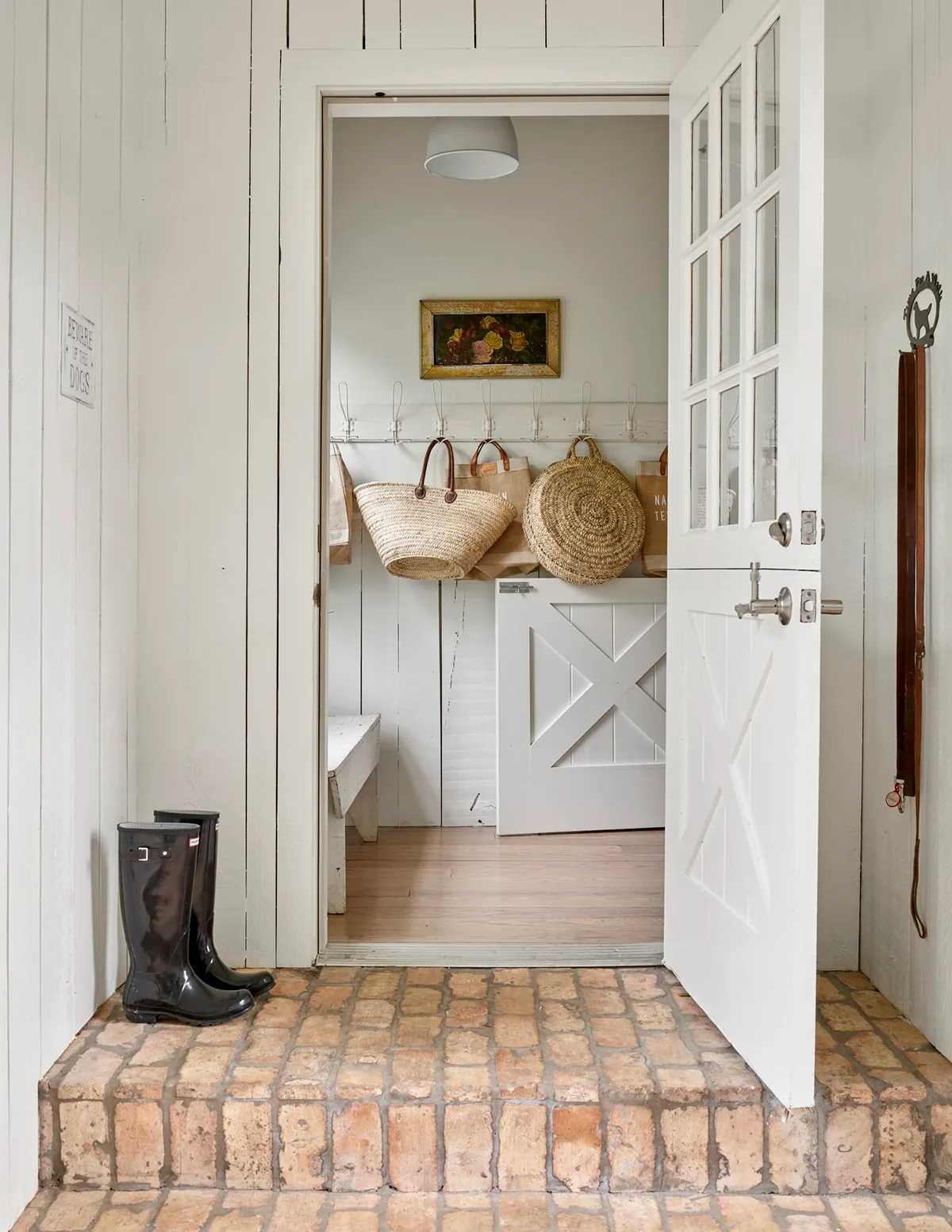 White divided glazed door at a brick-toned step leading to a paneled mudroom with baskets on a peg rail.