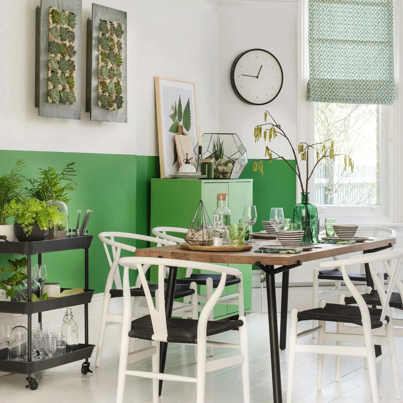 Bright green lower walls and a cabinet sit behind a wooden dining table, white chairs and a patterned pale green blind