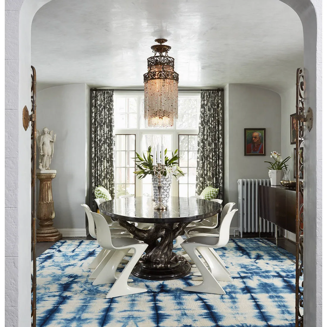 Blue and white patterned rug beneath a dark round dining table and white sculptural chairs