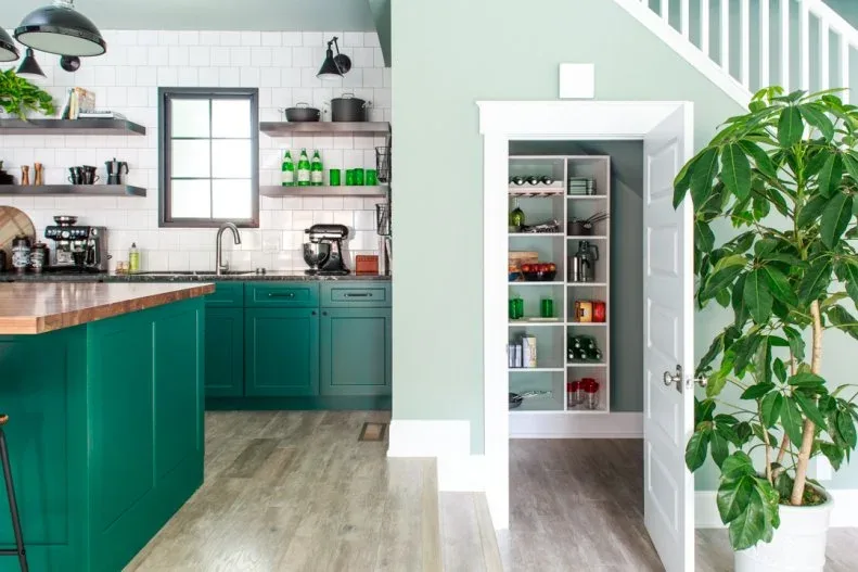 Green country kitchen with wood counter, open shelving and white-trimmed pantry doorway beneath stairs