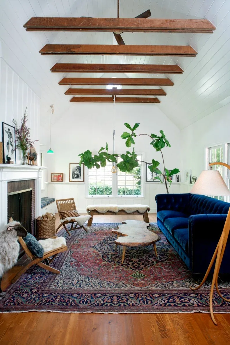 Blue sofa and open wooden chairs beneath exposed ceiling beams with a patterned rug and irregular table.