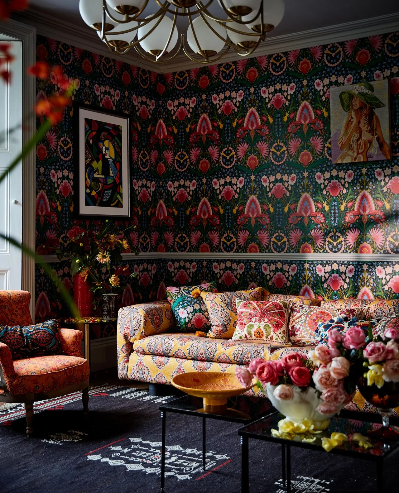 Dark patterned wallpaper surrounds a sofa with richly colored cushions and a low table.