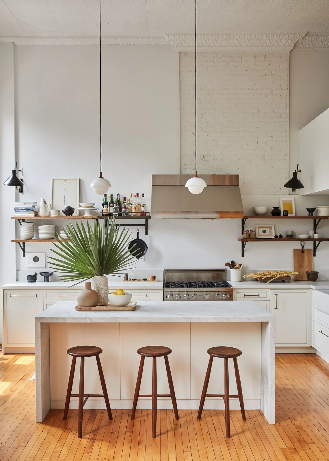 Pale kitchen cabinets and a light island sit beneath open shelves and metal lighting above a warm wooden floor