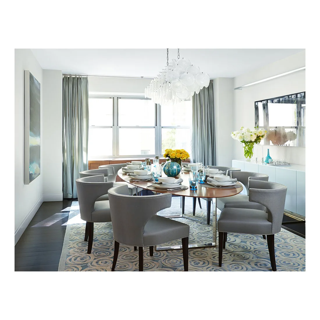 Oval dining table set with plates and glasses among gray curved-back chairs in a bright room