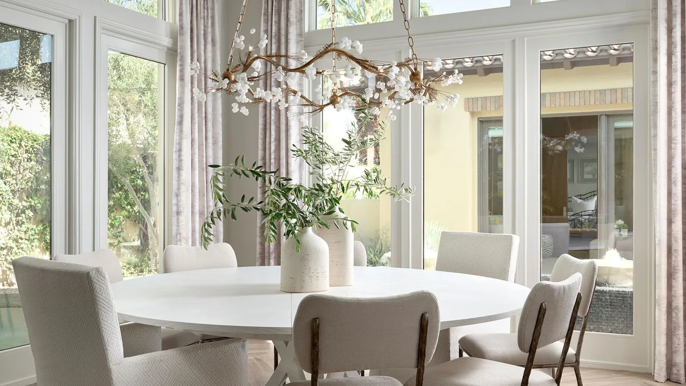 Round pale dining table with mixed upholstered chairs, glass doors and a branching decorative ceiling light.