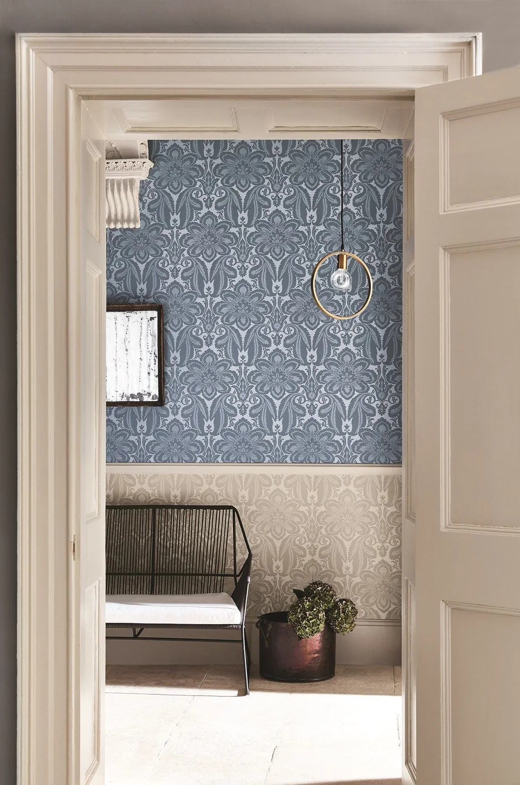 Blue patterned wallpaper sits above a pale related print separated by a white rail beside a black open-frame bench and a round plant pot