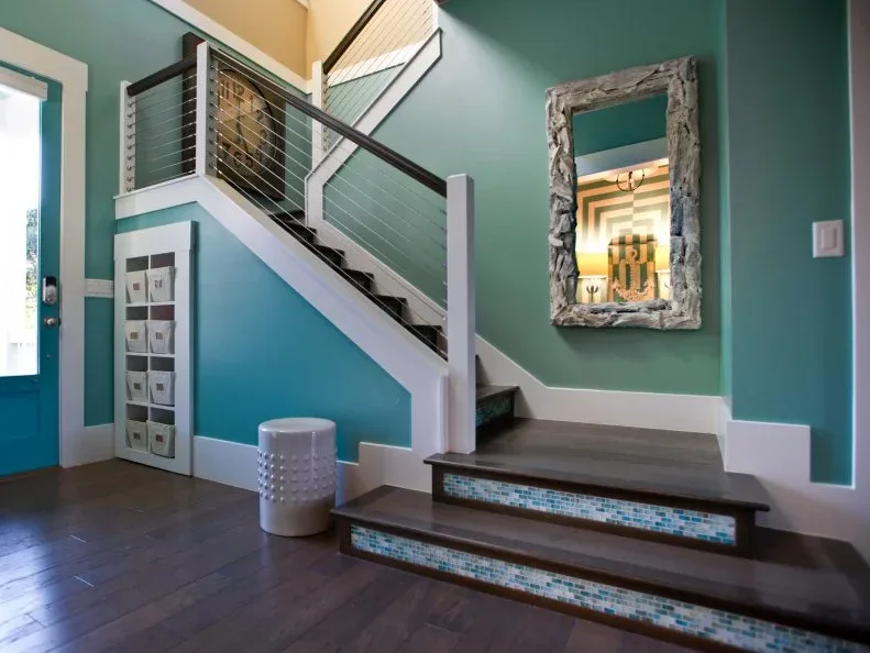 Aqua foyer with dark wooden stairs, blue-green tiled risers, white trim and tall decorative mirror.