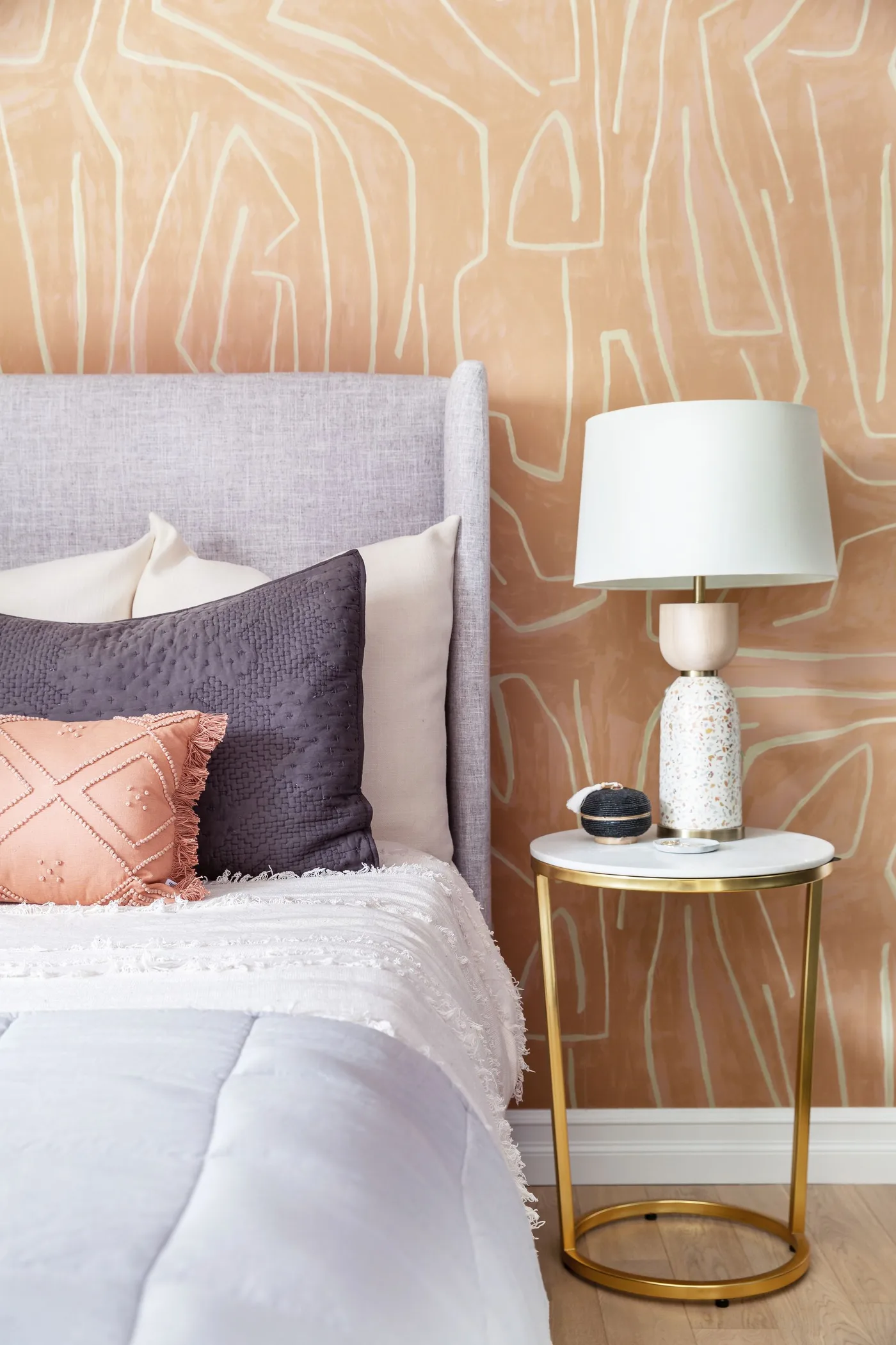 Clay-colored wall with pale abstract outlines behind a gray upholstered headboard and peach cushion