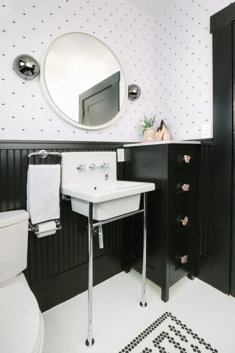 Black beadboard powder room with white open-leg washstand, round mirror and small-pattern wallpaper