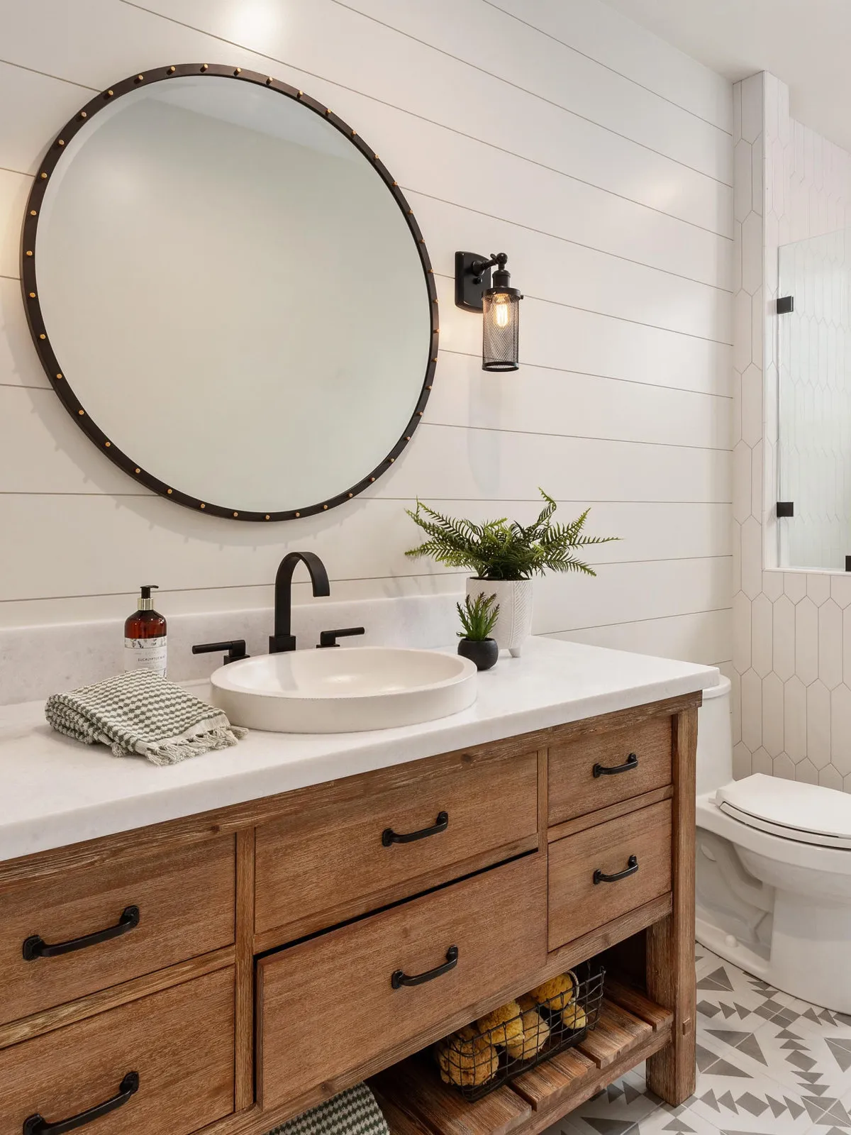 A round mirror hangs above a pale basin and timber vanity with open lower storage.
