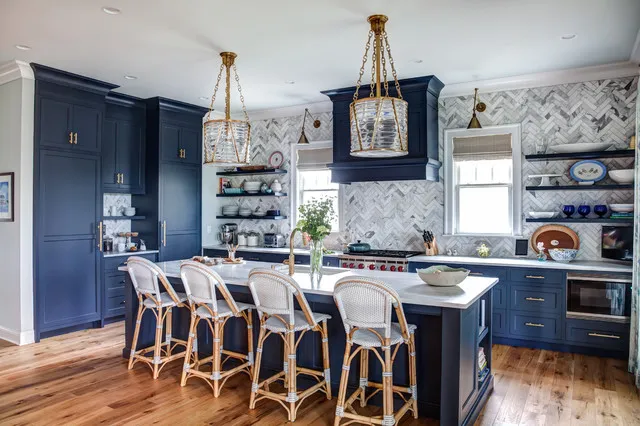 Navy cabinets and island surround pale counters beside woven-backed stools, patterned wall tiles and two warm-colored pendants