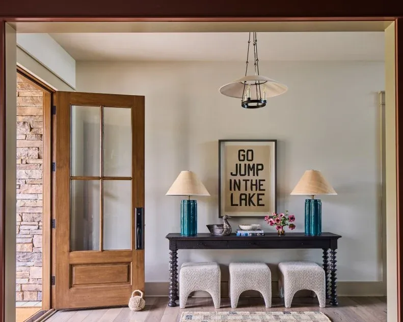 Country entry with broad shallow shade above candle-style lights, wood glazed door, dark console, blue lamps and three tucked stools