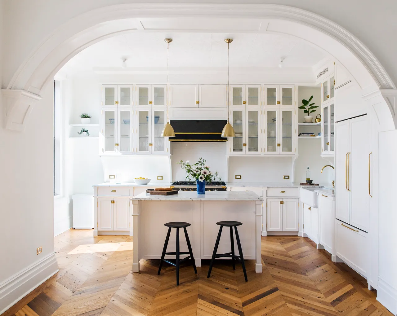 White kitchen cabinets and a pale island above a warm herringbone timber floor