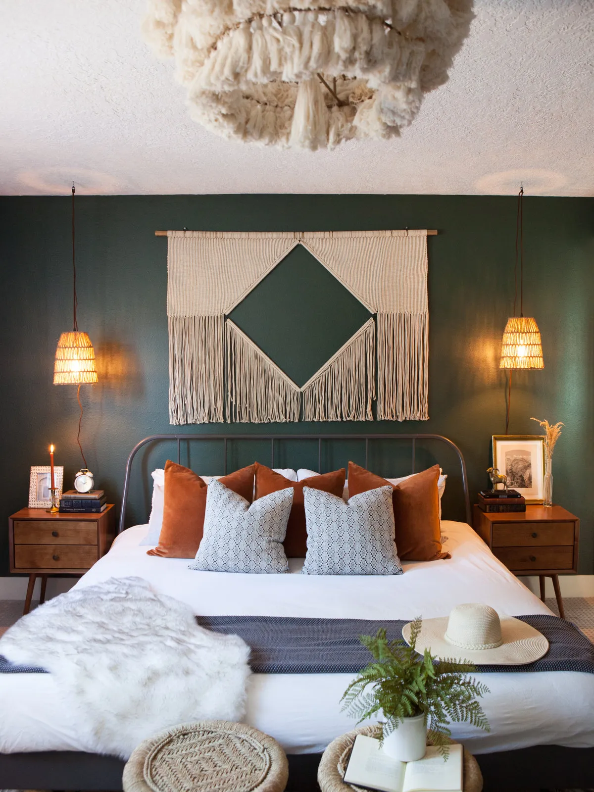 A deep green wall frames a pale bed beneath a layered natural pendant.