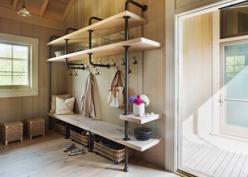 Wood-paneled mudroom with pale wooden bench and shelves, dark pipe-shaped supports, hooks and woven baskets below.