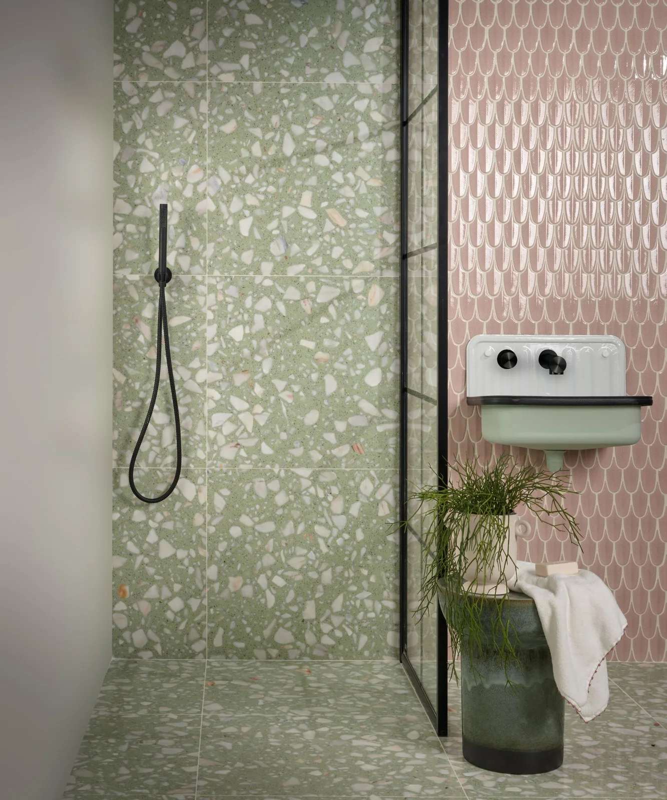Speckled green shower walls and floor meet pink scalloped wall tiles behind a pale green wall-mounted basin and black fittings