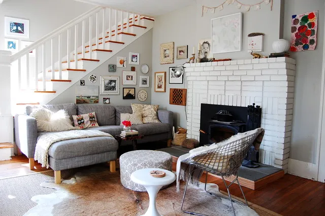Pale modular seating faces a small white table beside a woven chair and brick fireplace.