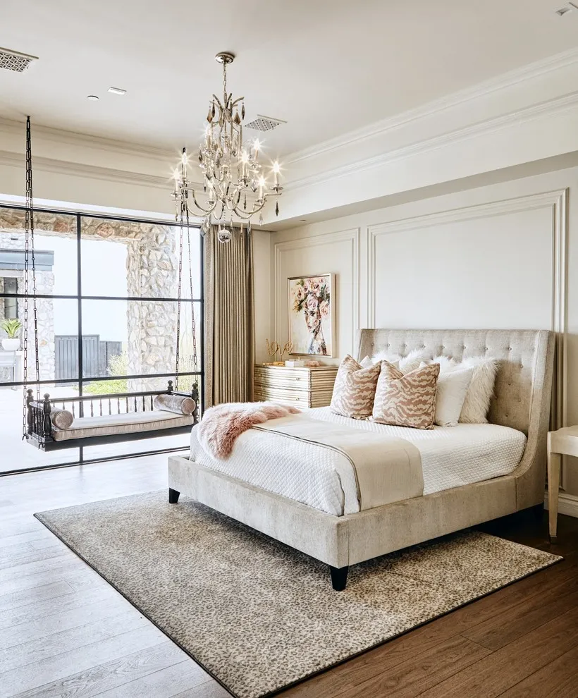 A beige upholstered bed sits beside a broad black-framed window and a pale rug