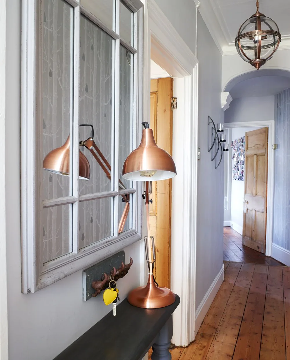 Narrow dark console with copper-toned adjustable lamp beneath a windowpane-style mirror and small wall key hooks