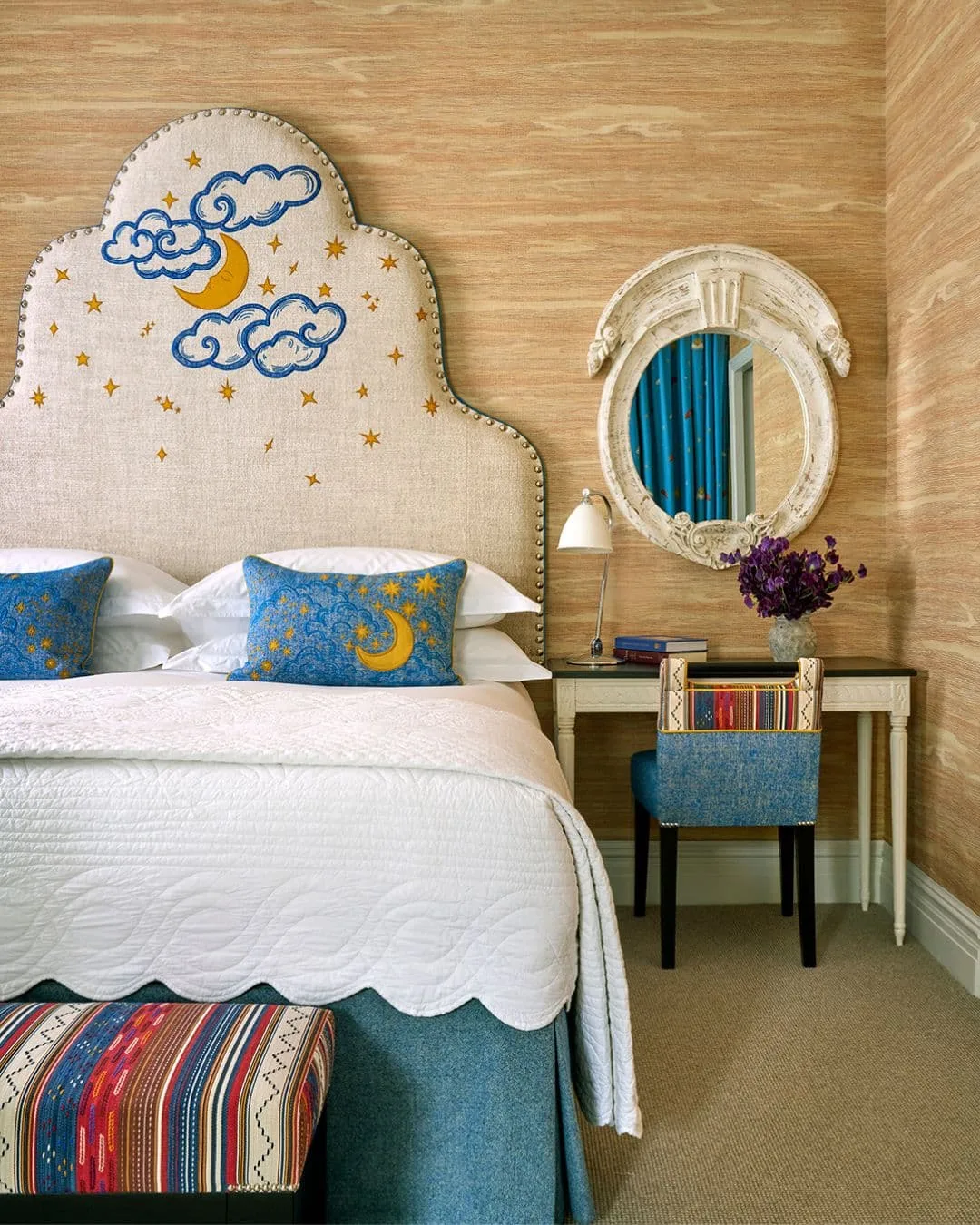 Pale shaped headboard decorated with a yellow crescent moon, blue clouds and stars beside an ornate mirror.