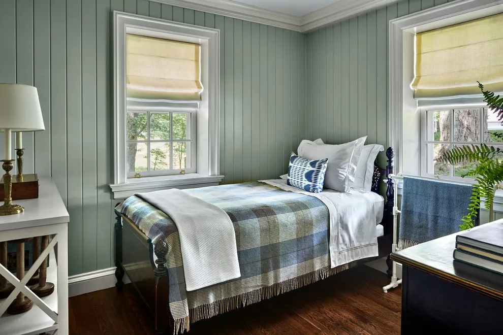 Gray-green vertical boards surround a narrow bed with checked bedding between two windows