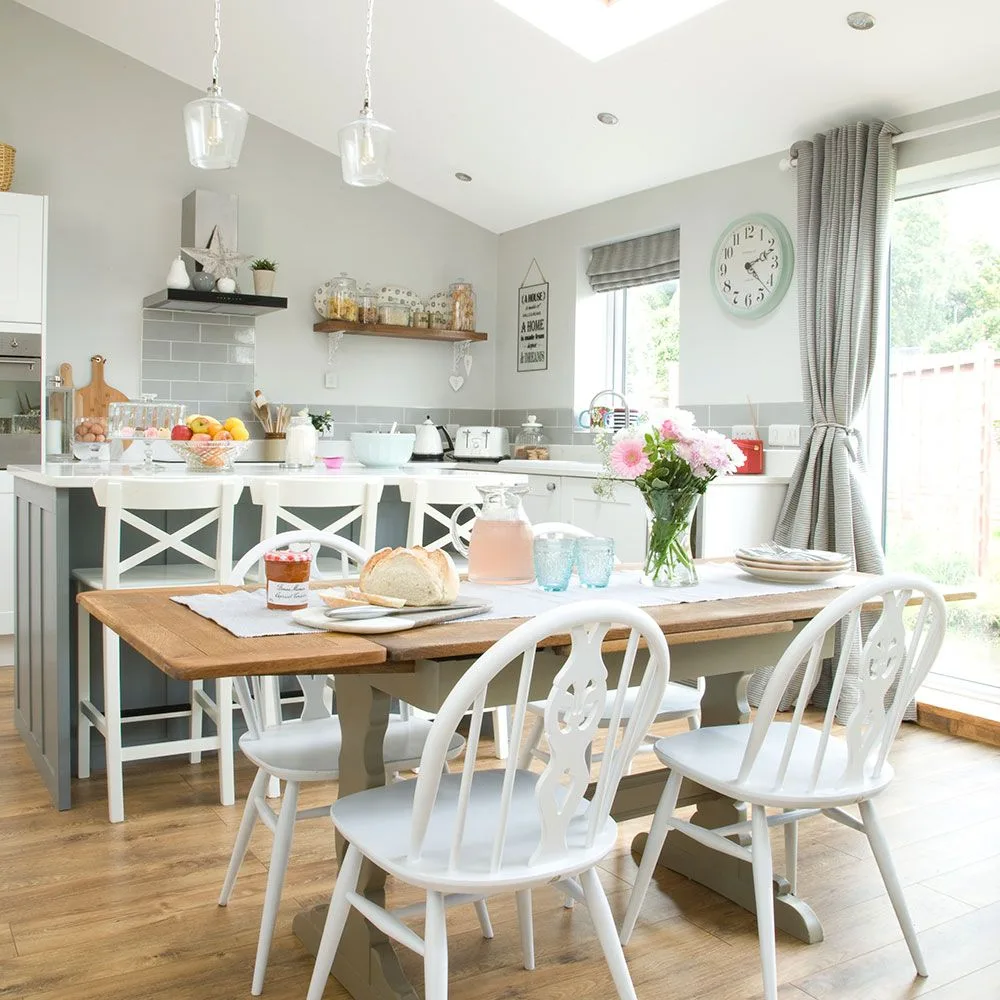 Gray patterned curtain tied beside a glazed opening in a kitchen dining area, with a matching-toned blind, wooden table, and white seating.