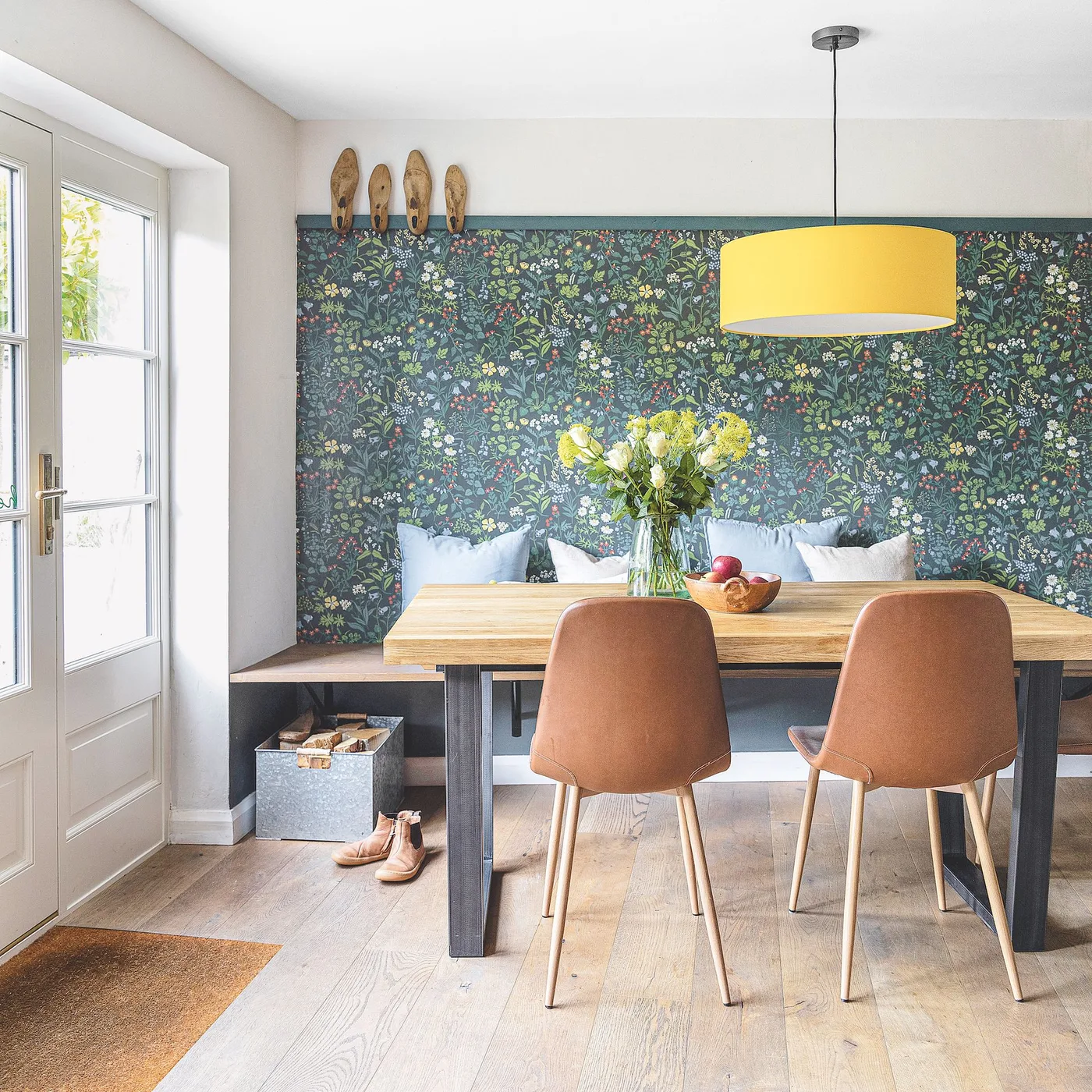 Yellow drum pendant above a wood table with tan chairs and a built-in bench against floral wallpaper