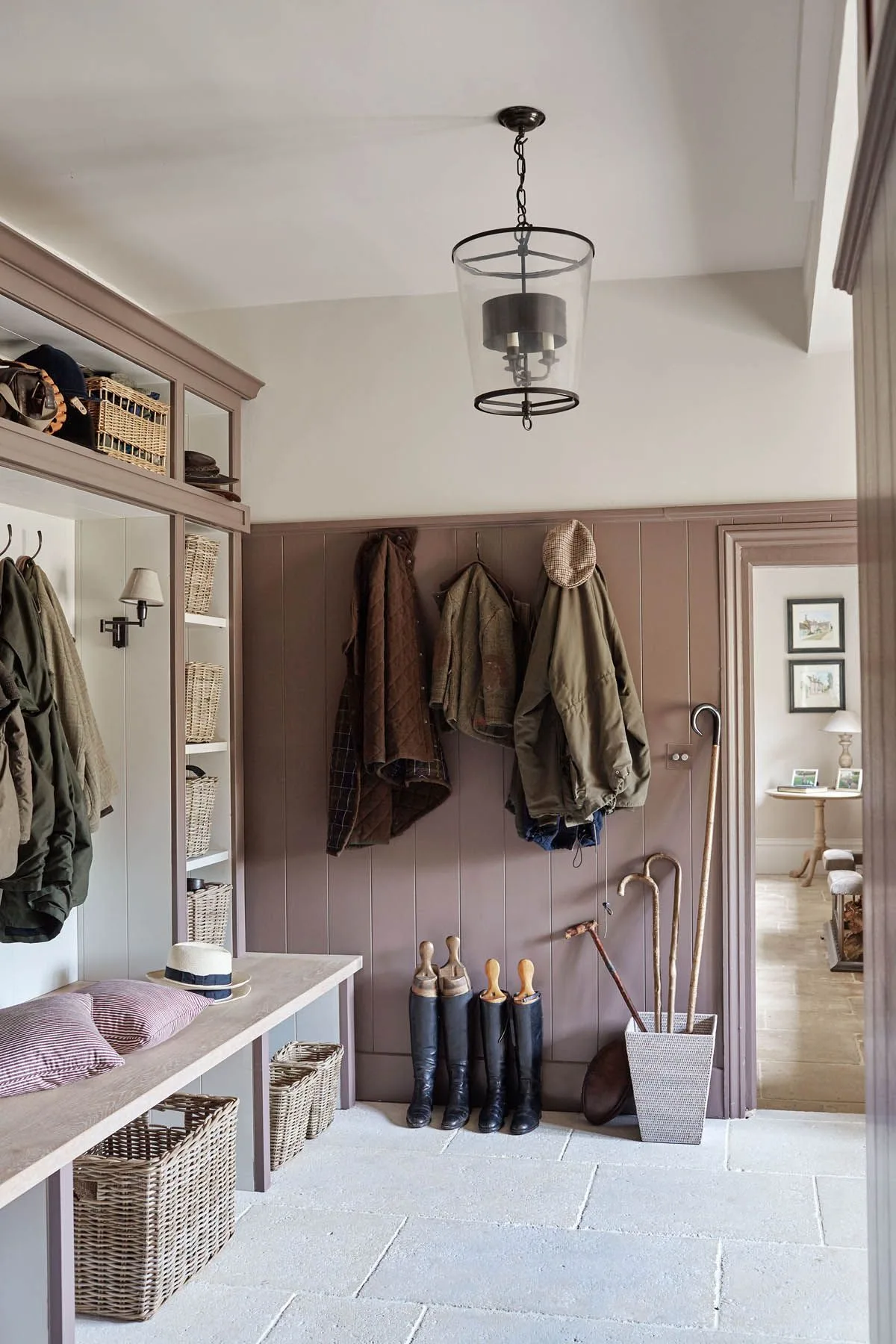 Muted purple mudroom with bench baskets, wall hooks, tall boots and a separate upright holder for walking sticks
