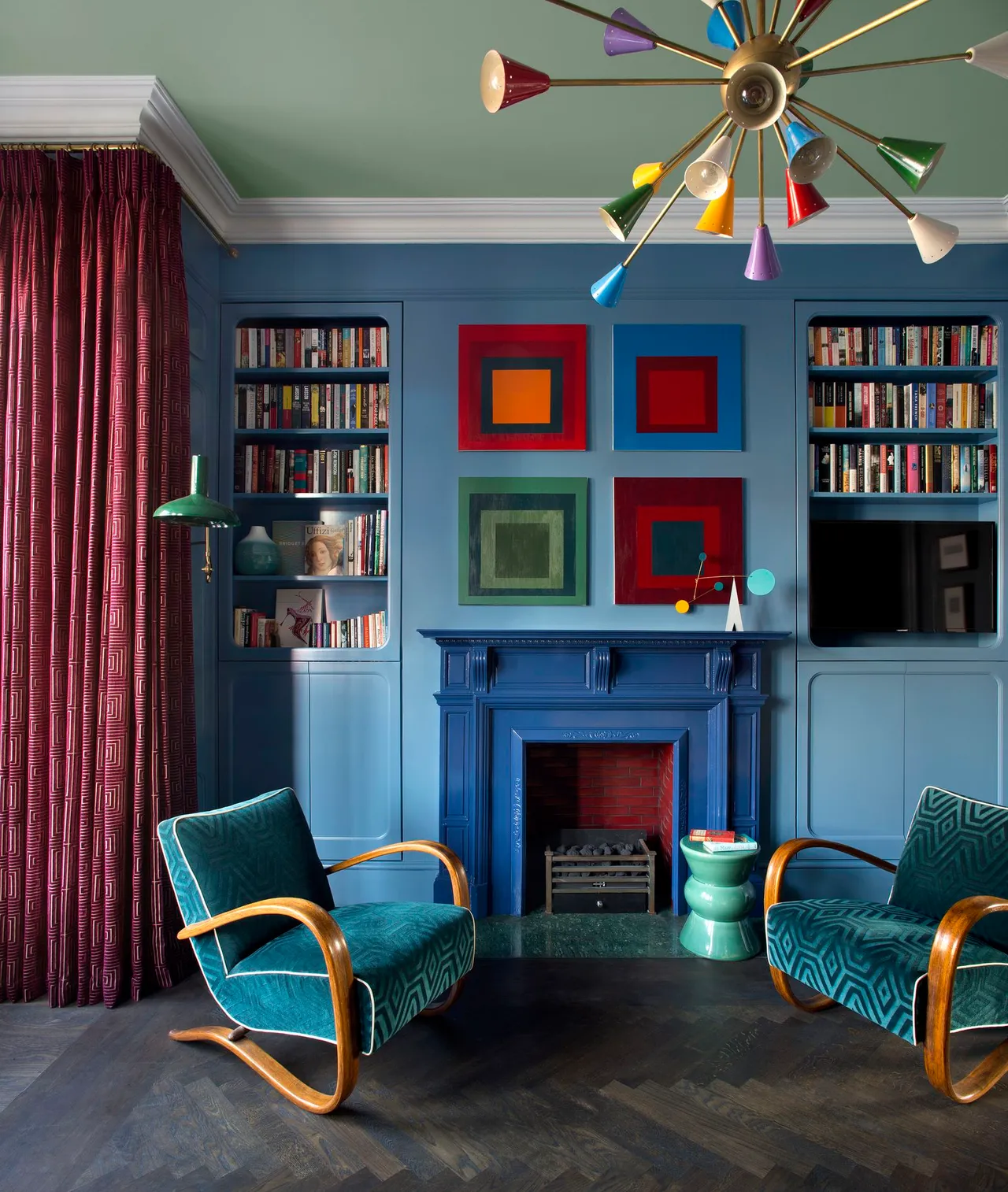 Blue walls and shelves surround warm framed artwork and green chairs.