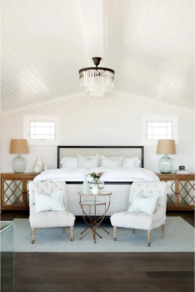 A pale bed and two chairs sit on a light blue rug above dark flooring