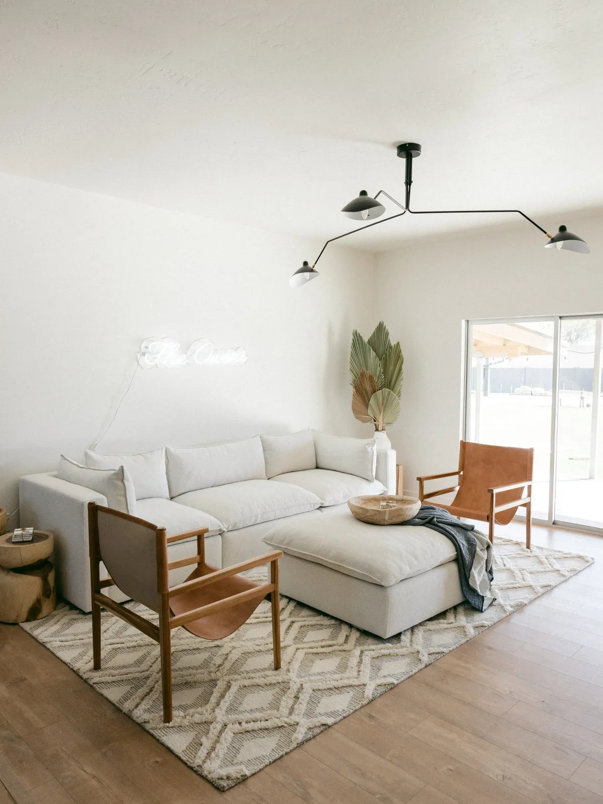 A pale sectional sits beside a timber-framed chair on a lightly patterned rug.