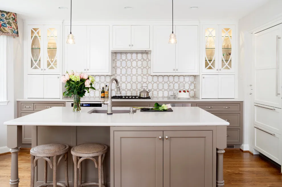 A taupe island with pale stools stands against a backdrop of white cabinetry