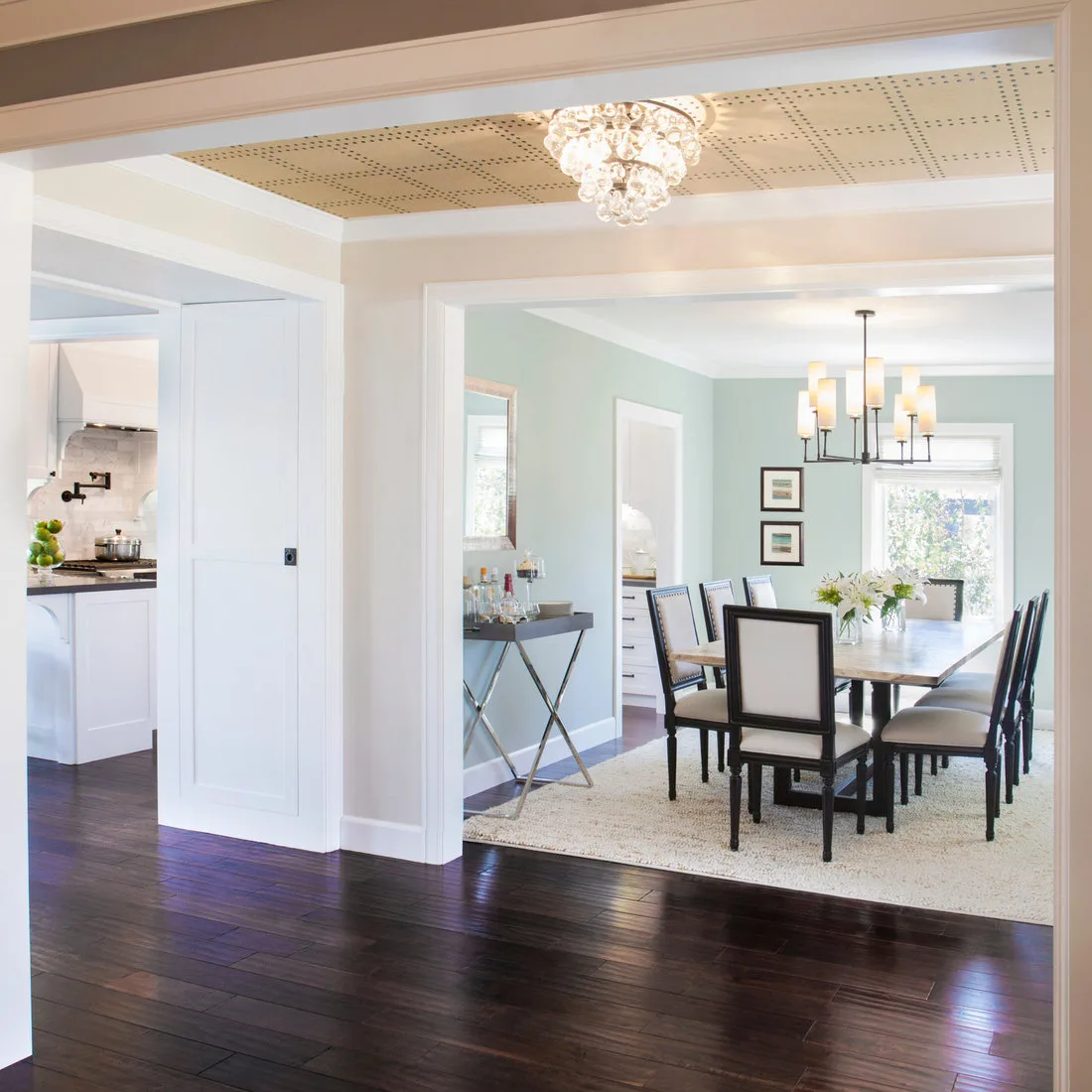 Pale textured dining rug beneath cream chairs and a wood table beyond a wide white doorway