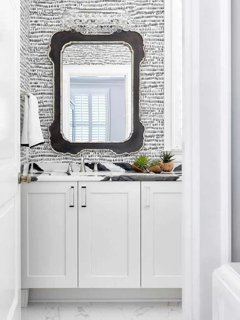 White powder-room vanity with shaped dark mirror, black-and-white patterned wallpaper and veined counter