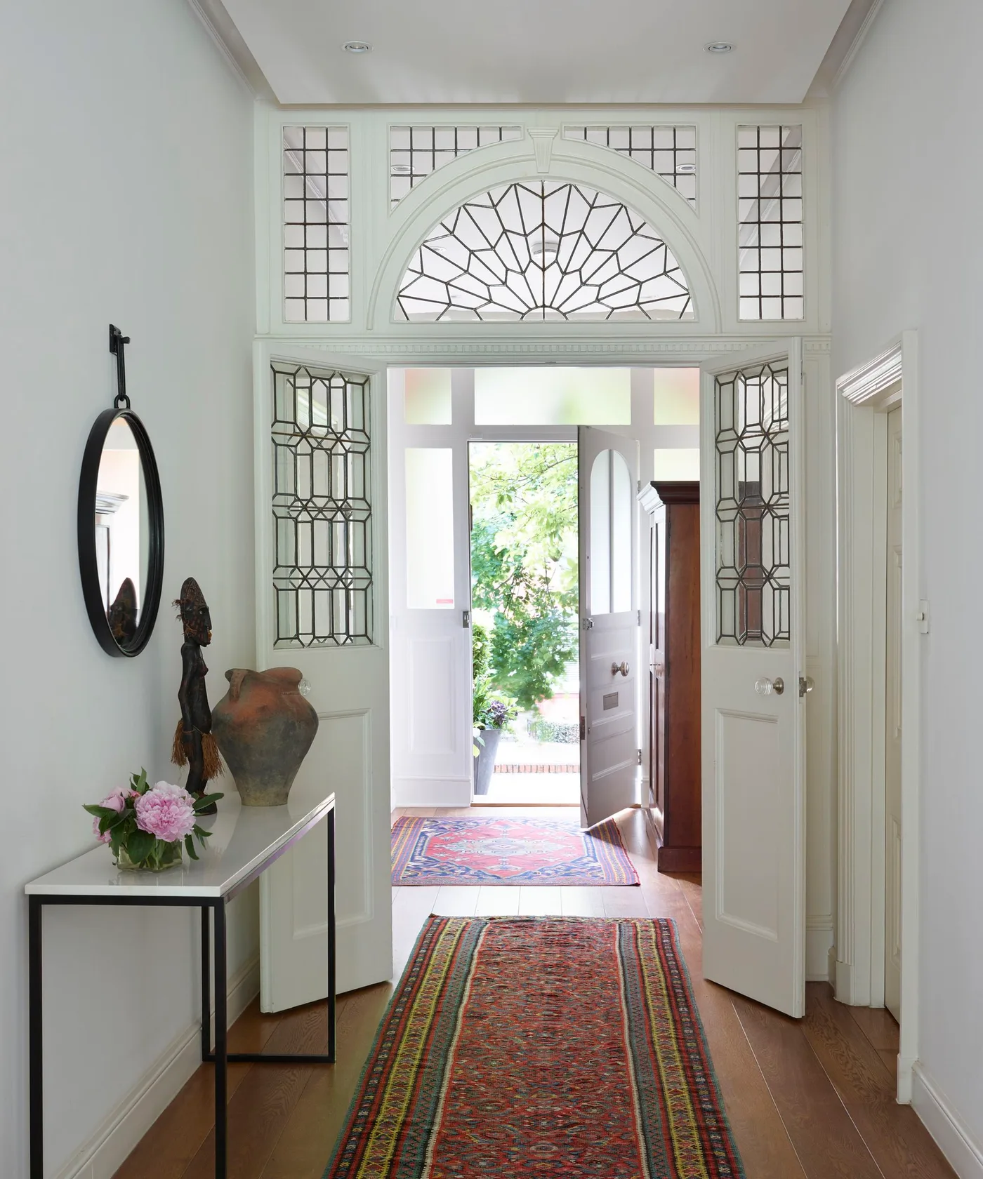 Red patterned runner and a separate colorful entrance rug on wood flooring beneath a decorative glazed arch