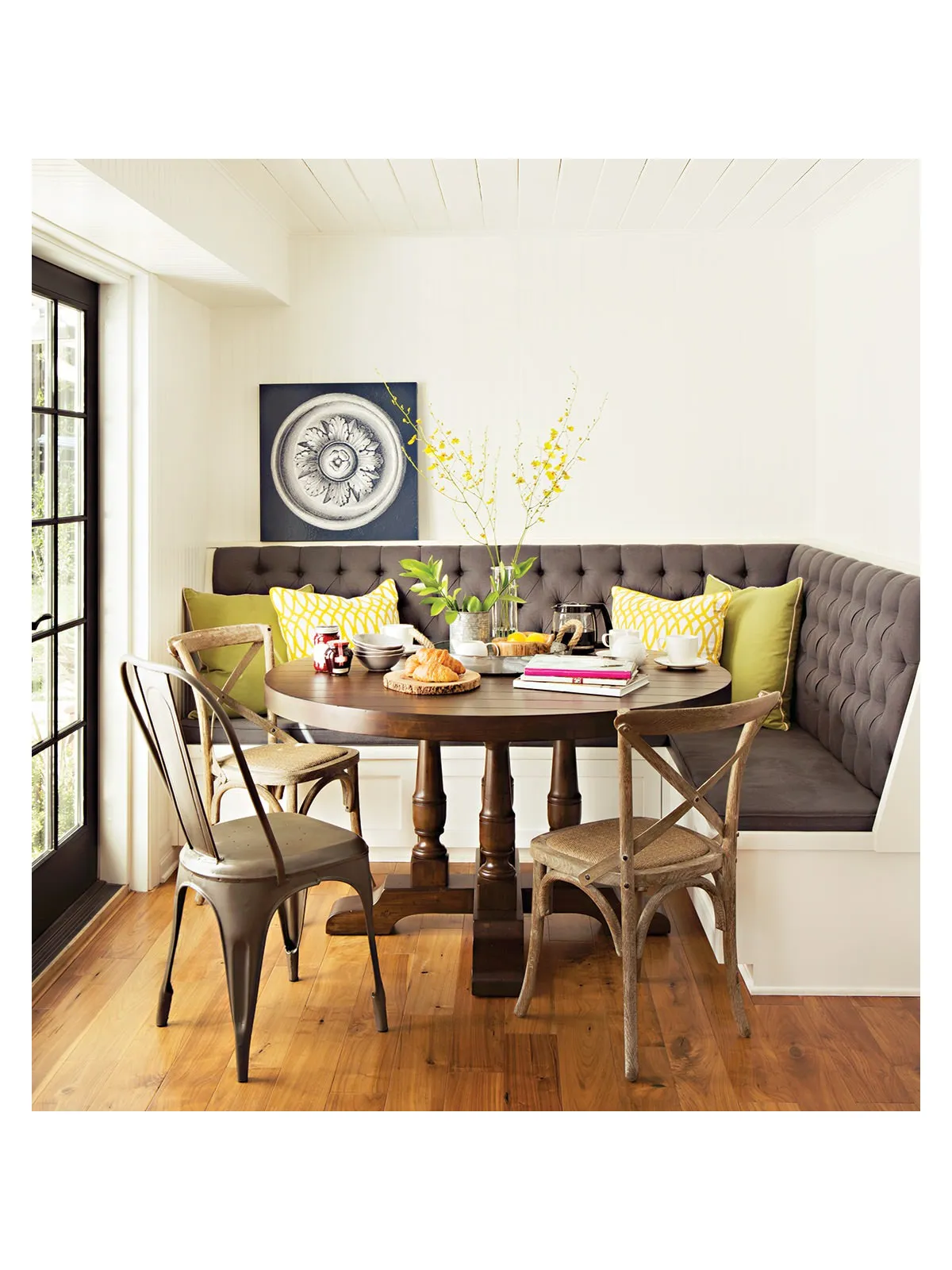 A tufted corner bench sits behind a small timber dining table and cross-back chairs.