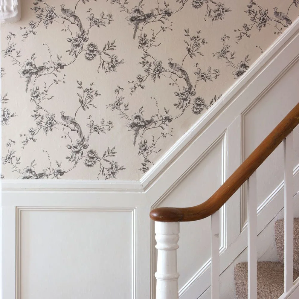 A fine gray botanical wall pattern follows the stairs above white lower paneling beside a warm-colored handrail and pale carpet
