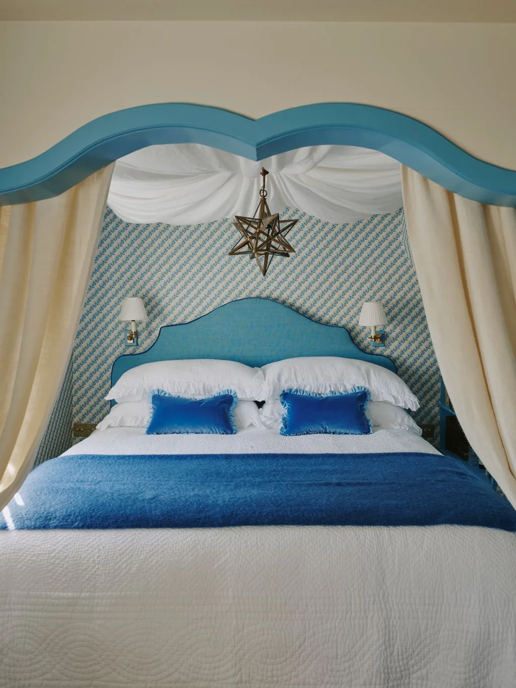 Bedroom with blue double-curved bed recess, matching headboard, cream curtains, blue-patterned backdrop and suspended star-shaped light