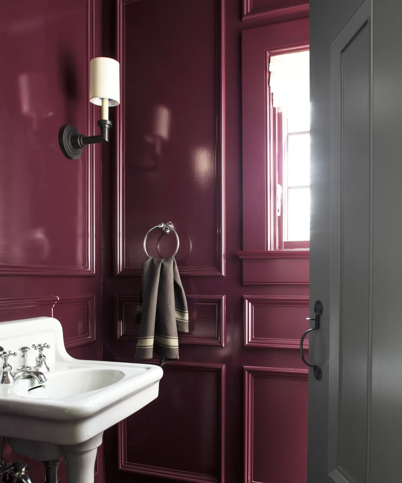 Burgundy paneled powder room with white pedestal basin, shaded black wall light and towel ring