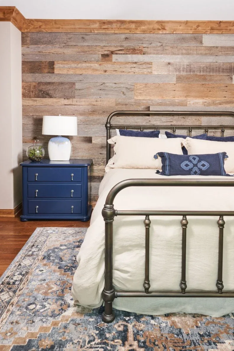Bedroom with weathered horizontal wood bed wall, dark metal bed and blue bedside chest