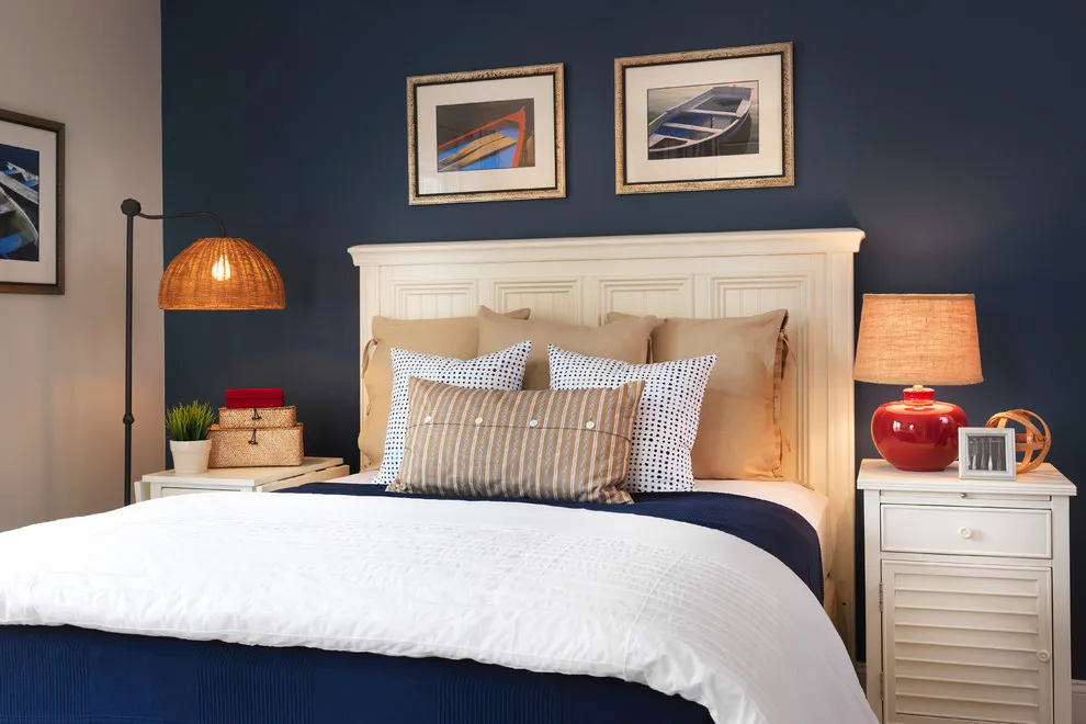 A navy wall frames a white headboard and pale bedside chest beneath two small pictures