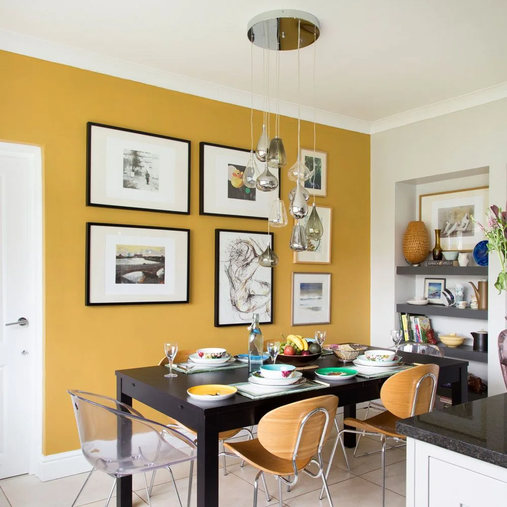 Cluster of small reflective drop pendants above a dark dining table against a mustard gallery wall