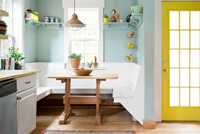 A small timber table and bench sit beside pale blue-green shelving and a vivid yellow glazed door.