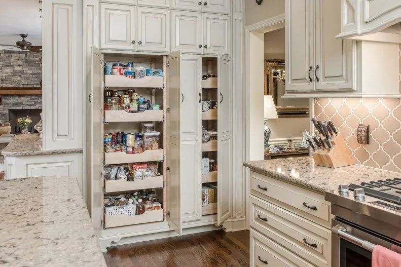 Traditional pale kitchen with tall pantry cabinet open to pull-out grocery shelves and neighboring narrow storage