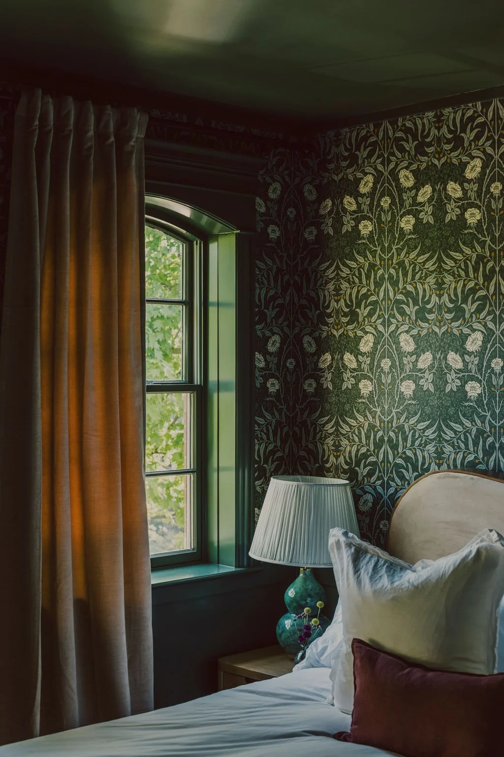 Bedroom with a forest green ceiling, dark green floral wallpaper, pale curved headboard, white bedding, green trim, and beige curtains.