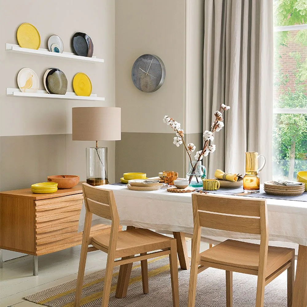 Two white plate ledges displaying yellow and neutral plates above a sideboard beside a wooden dining table