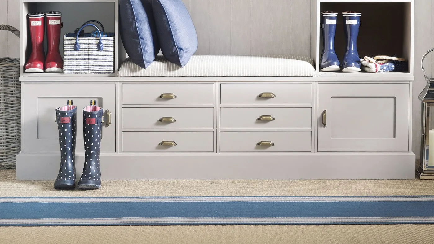 Blue-centered runner with pale and narrow dark borders in front of a light mudroom bench with drawers, cubbies and boots