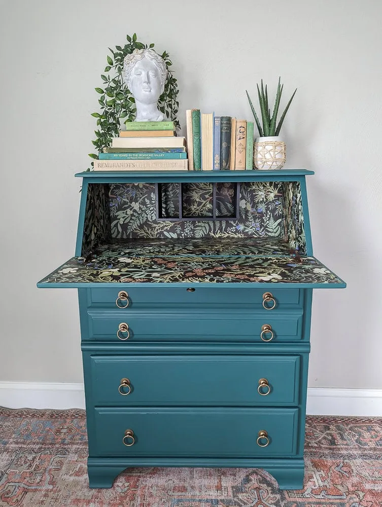 Open blue-green secretary desk with a leafy patterned interior and gold-toned ring drawer pulls.
