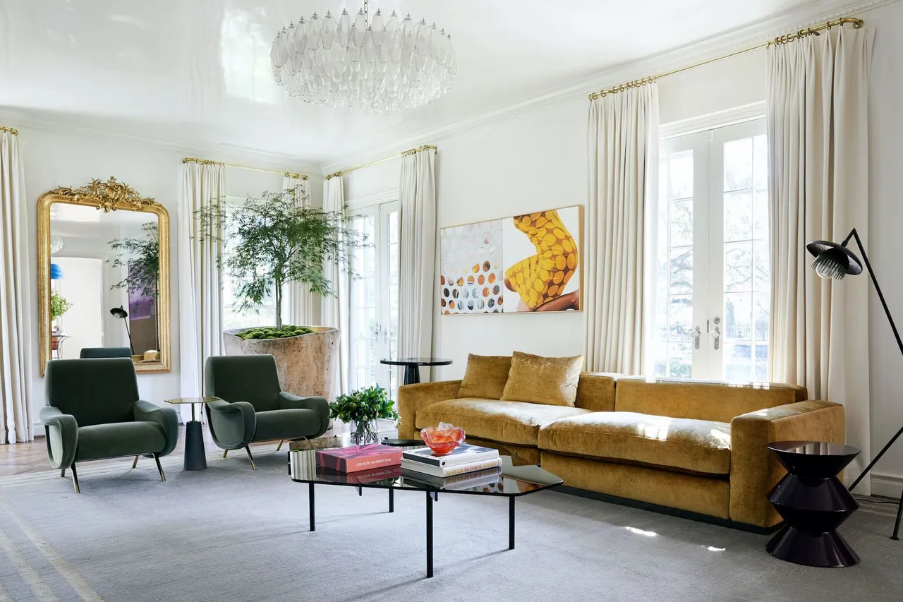 Gold sofa and two dark green armchairs in a bright room beside a large ornate mirror